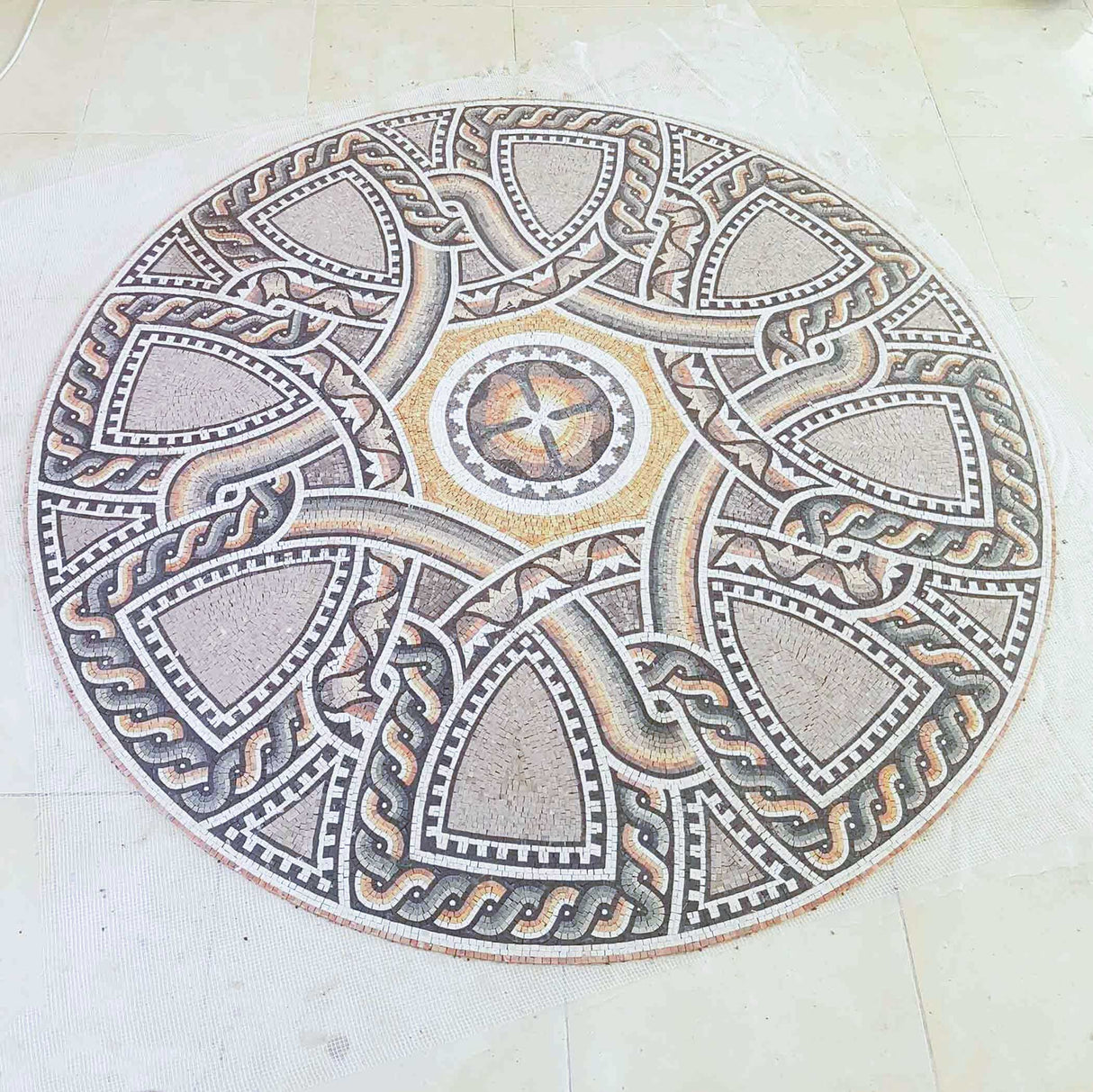 Perspective angle view of a hand-cut earth tone geometric marble mosaic medallion on mesh backing before installation.
