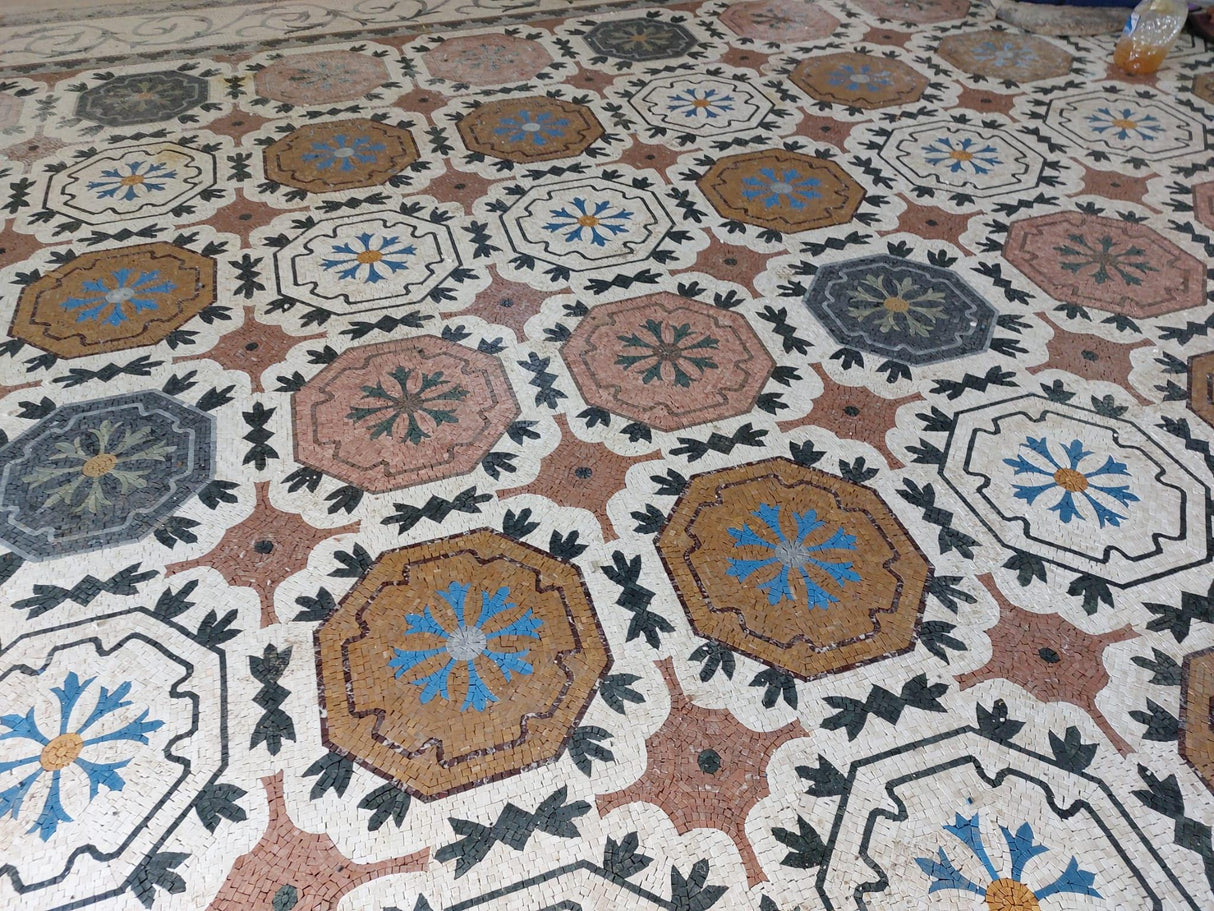 Close-up shot of hand-cut natural marble mosaic octagonal medallions with detailed ochre gold and terracotta rosettes.