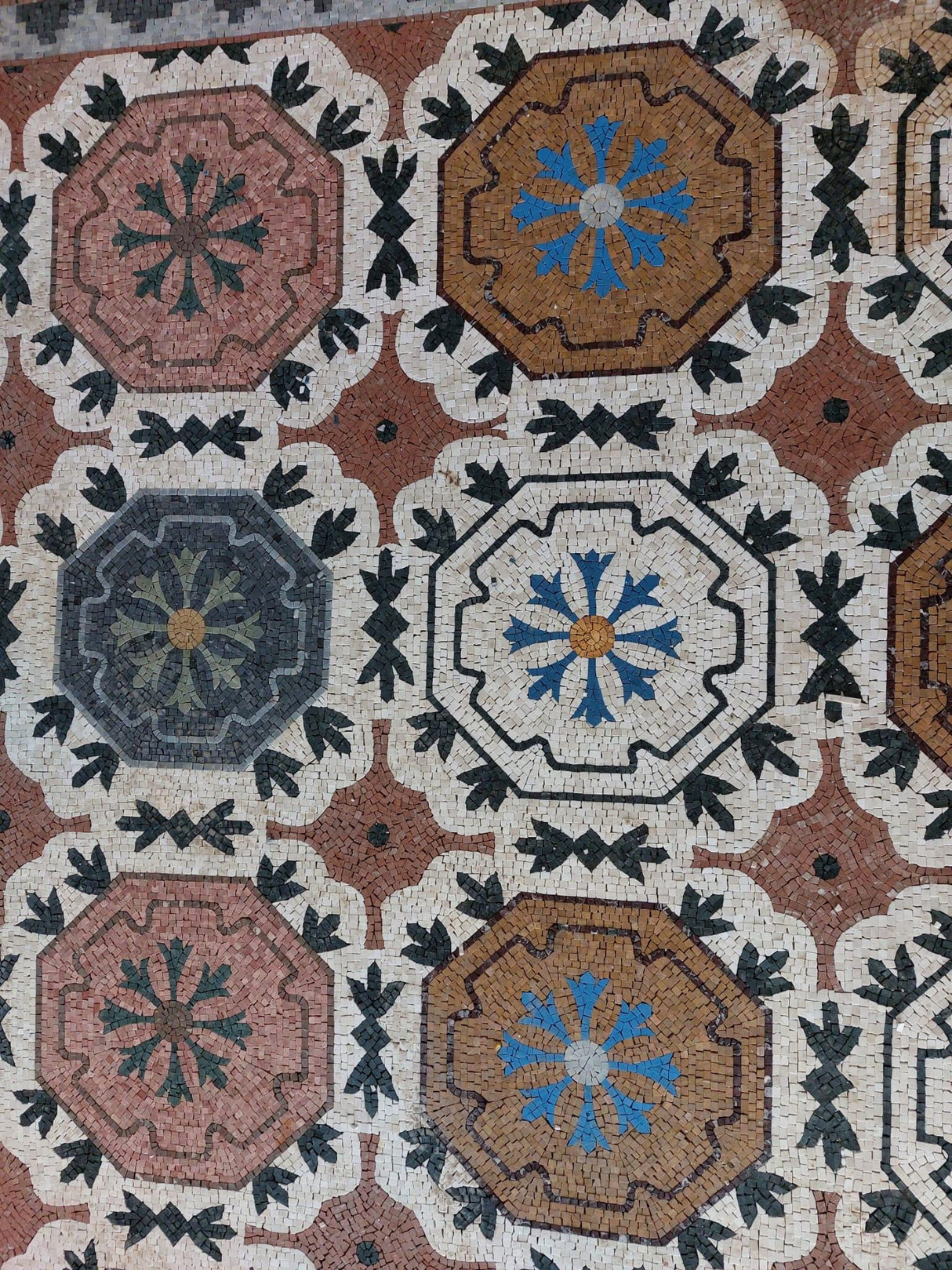 Luxury entry floor inlay showcasing the rich natural colors of terracotta, rose, and gold marble mosaic tiles.