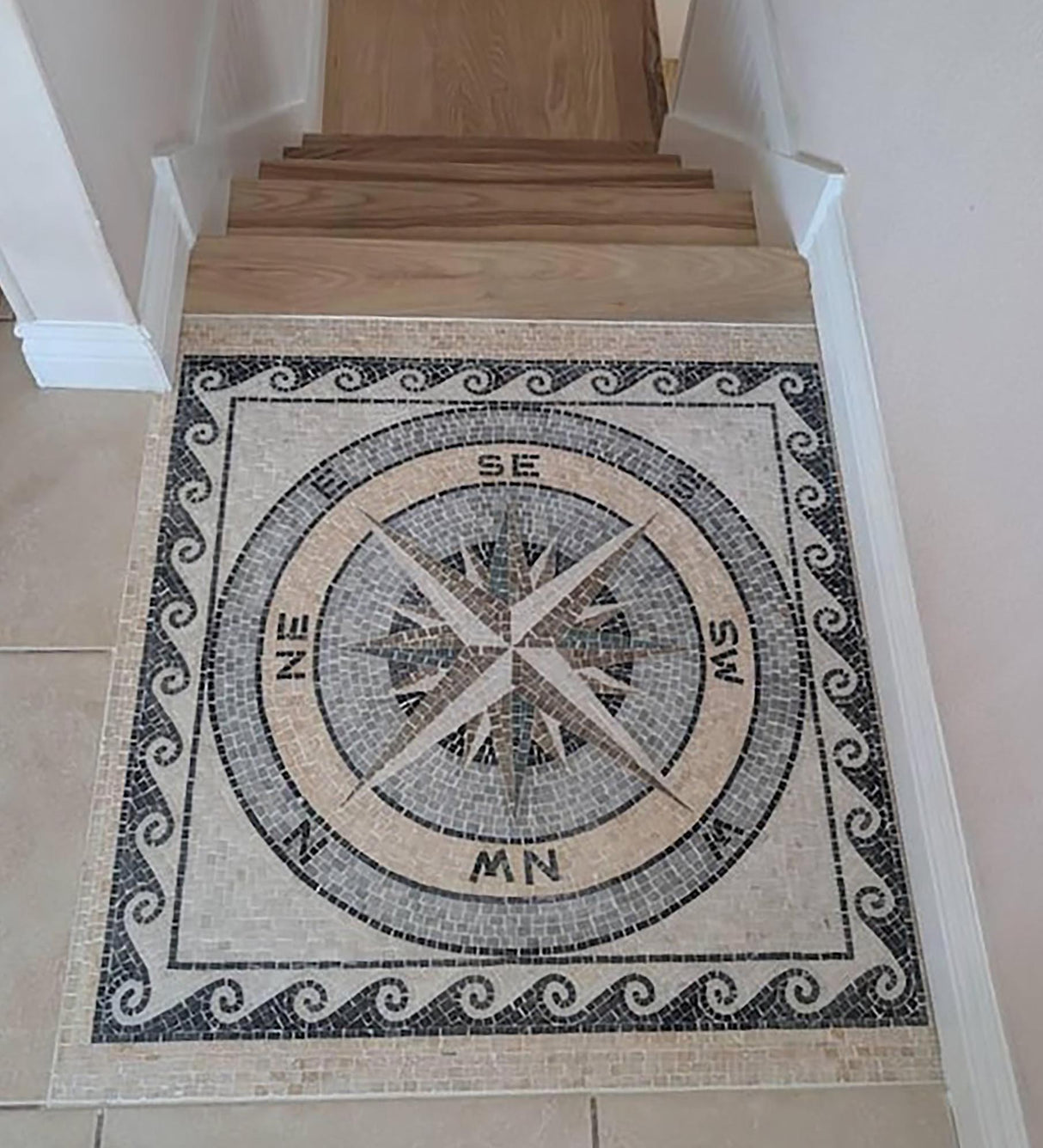 Residential staircase landing floor featuring a custom handcrafted nautical compass rose square marble mosaic medallion with a running wave border.