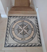 Residential staircase landing floor featuring a custom handcrafted nautical compass rose square marble mosaic medallion with a running wave border.